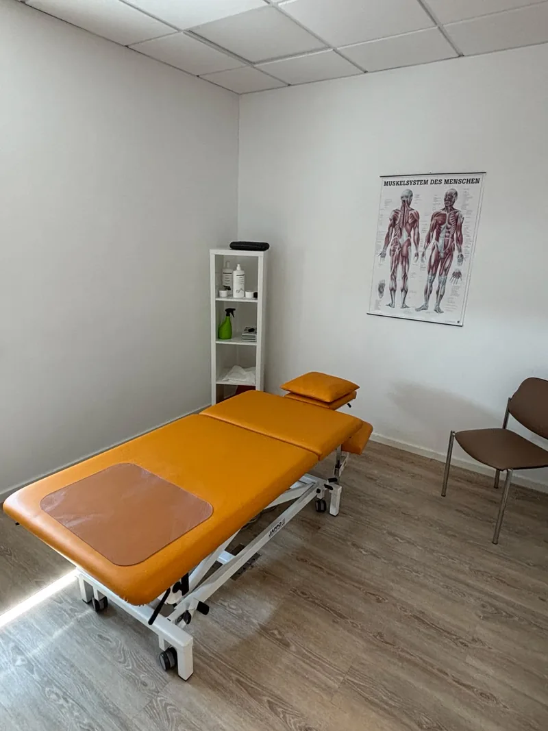 Behandlungsraum mit Liege, Wandposter des Muskelsystems und Stuhl