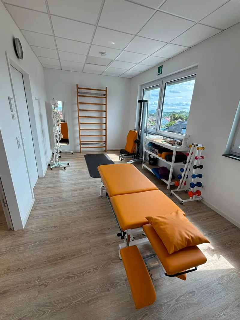 Behandlungszimmer mit Liege, Sprossenwand, Anatomiemodell und Hantelablage